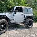Gray Jeep Rubicon with large off-road tires on a paved road with greenery in the background