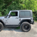 Gray Jeep Wrangler Rubicon parked on a gravel road with greenery in the background