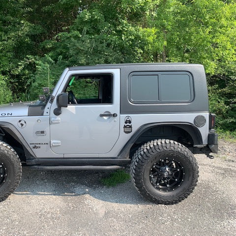 Gray Jeep Wrangler Rubicon parked on a gravel road with greenery in the background