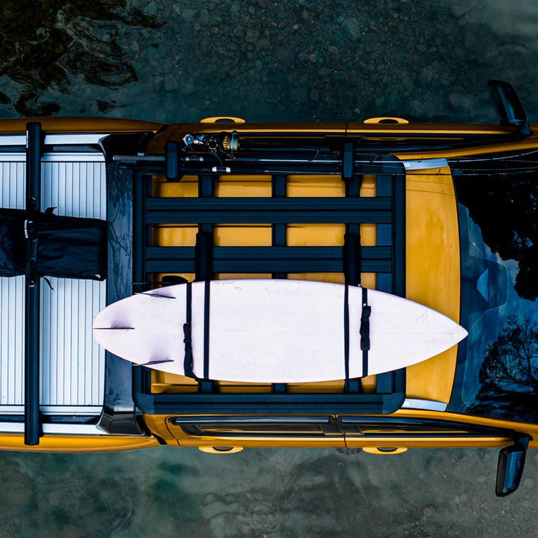 Top-down view of a car with a surfboard on a roof rack over water.