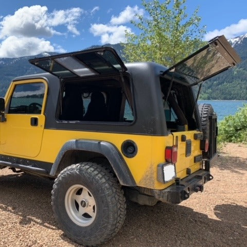 Yellow off-road vehicle with open doors parked near a lake with mountains in the background