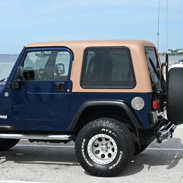 Blue Jeep Wrangler with tan roof parked in a lot near water