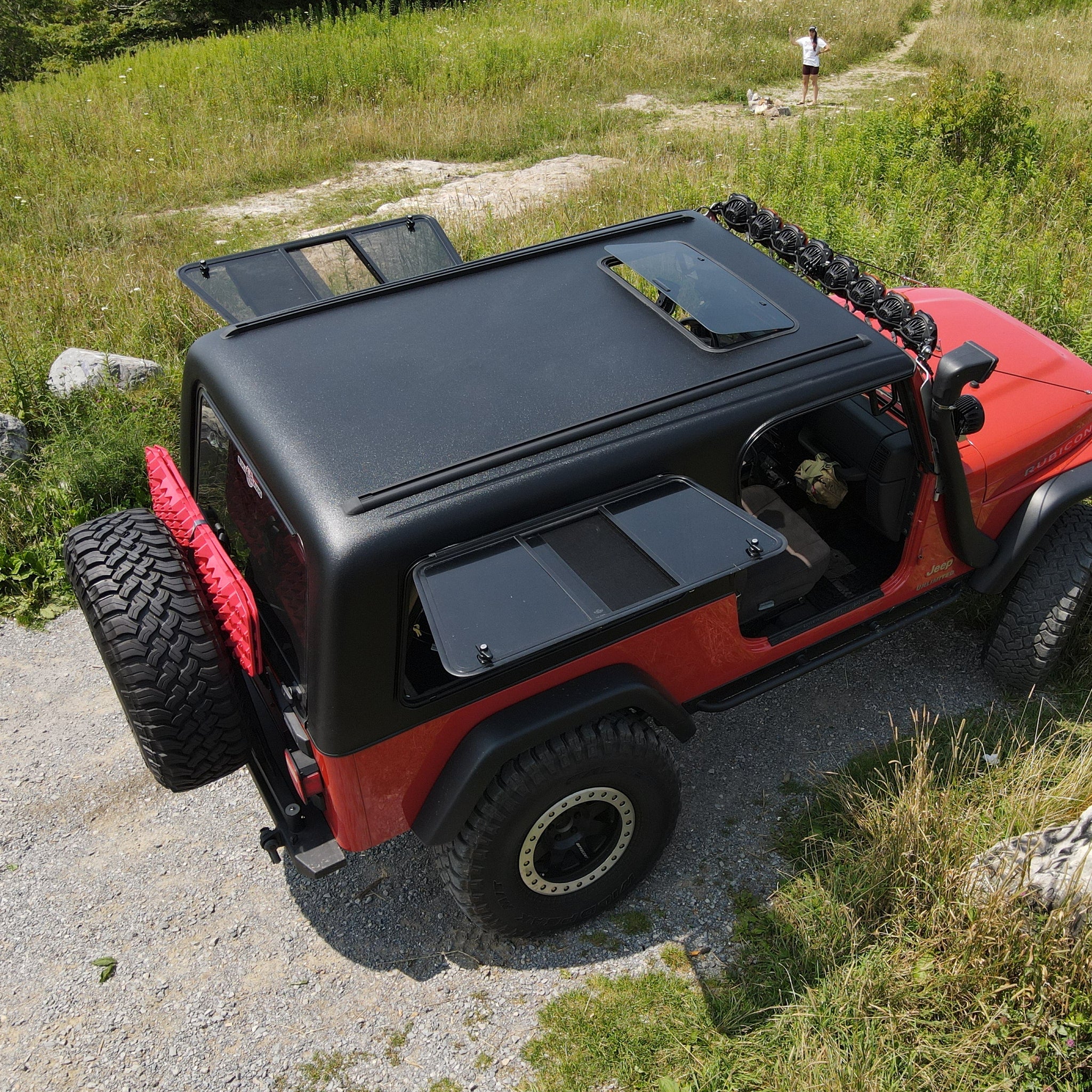 Red off-road Jeep with black roof rack on a rocky path