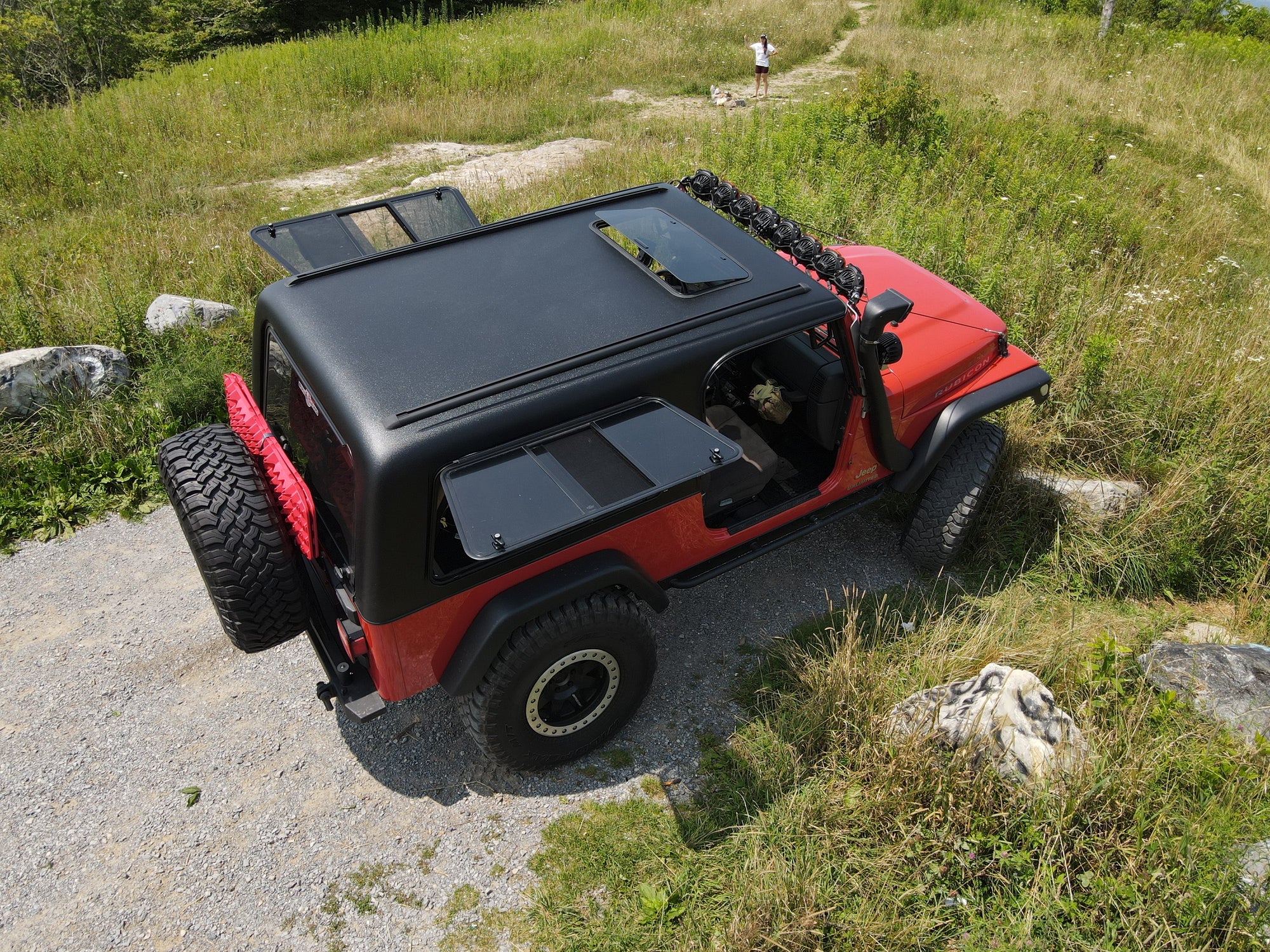 Red off-road vehicle with black roof rack on a rocky path