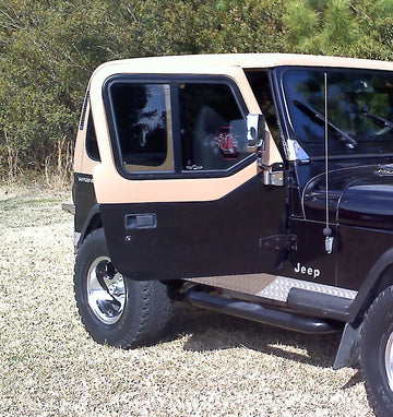 Black Jeep Wrangler parked on a gravel surface with greenery in the background