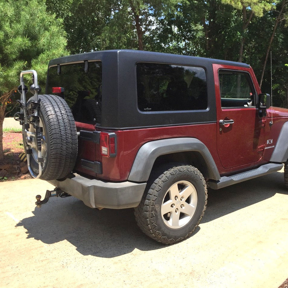 Red Jeep Wrangler with black soft top parked on a paved road with trees in the background