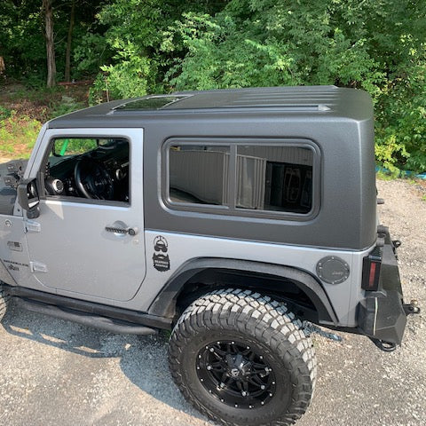 Red Jeep Wrangler with black soft top parked on a paved road with trees in the background