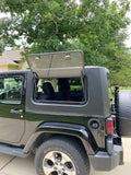 Silver Jeep with open door in a driveway with trees in the background
