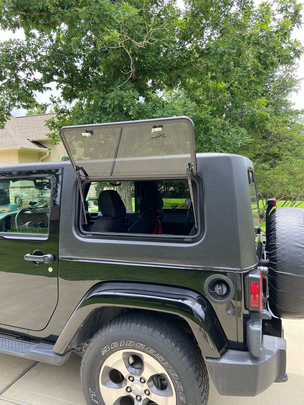 Silver Jeep with open door in a driveway with trees in the background
