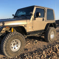 Beige Jeep Wrangler on a rocky terrain with a clear blue sky.