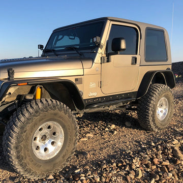 Beige Jeep Wrangler on a rocky terrain with a clear blue sky.