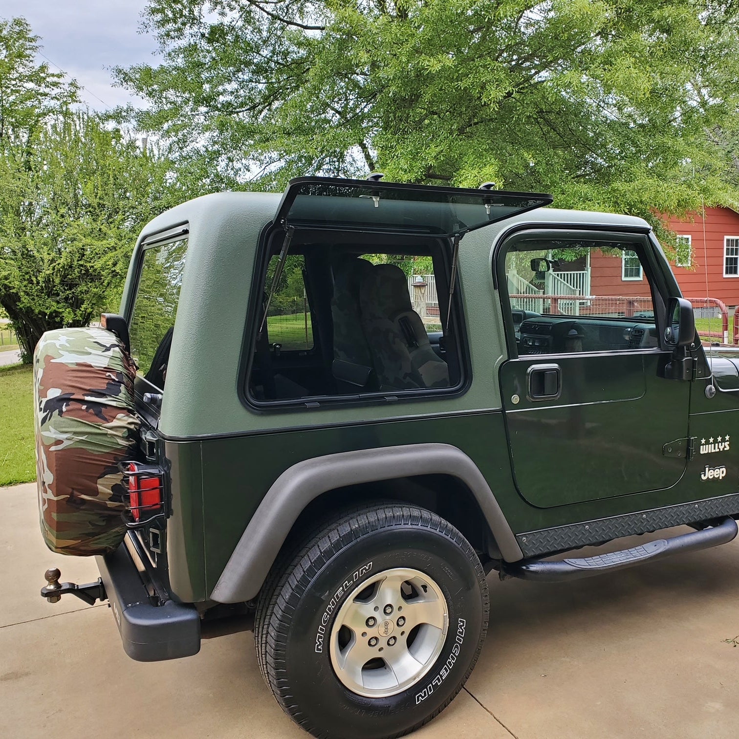 Green Jeep Wrangler parked on a driveway with trees and a house in the background