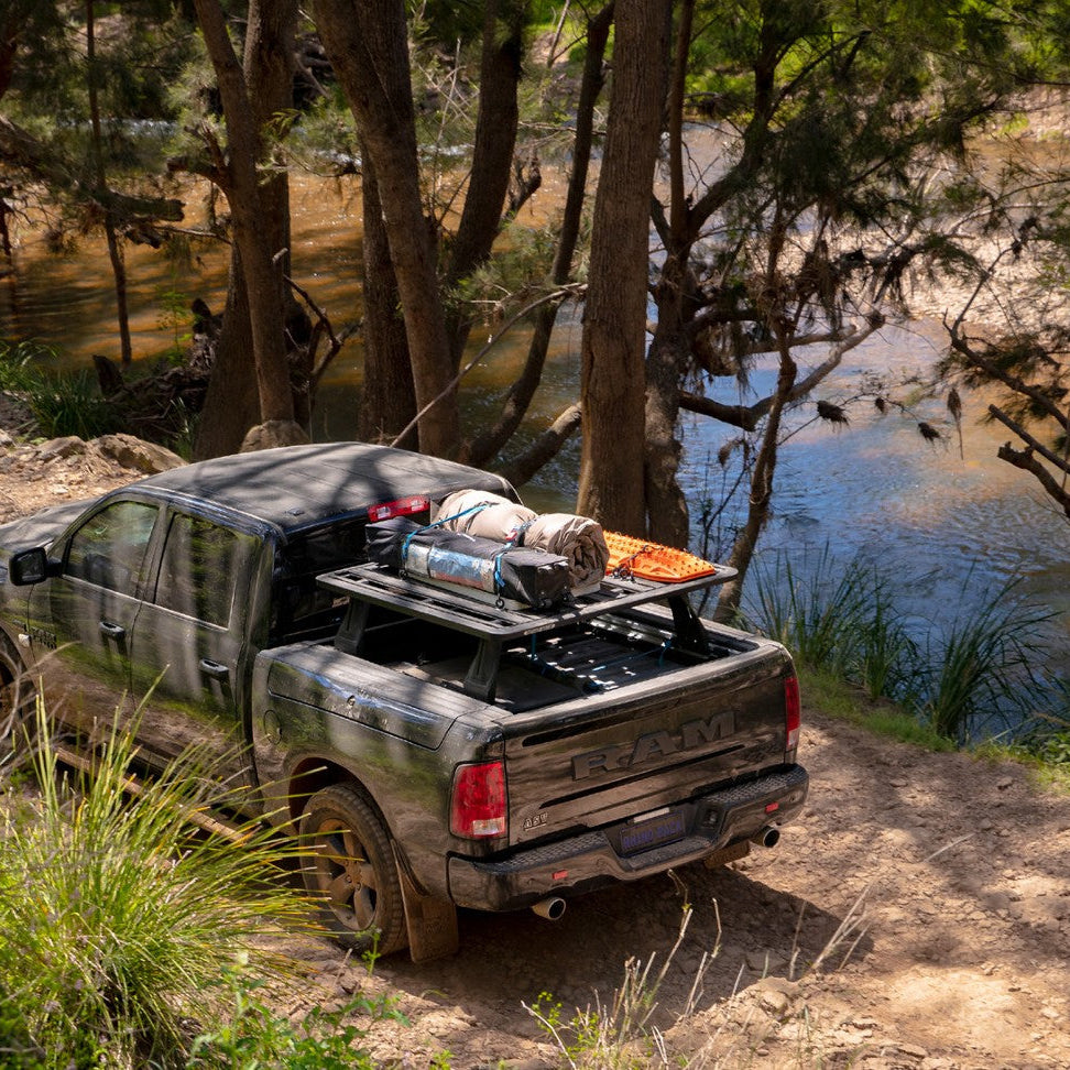 Truck with a bed rack loaded with camping gear parked by a lake.