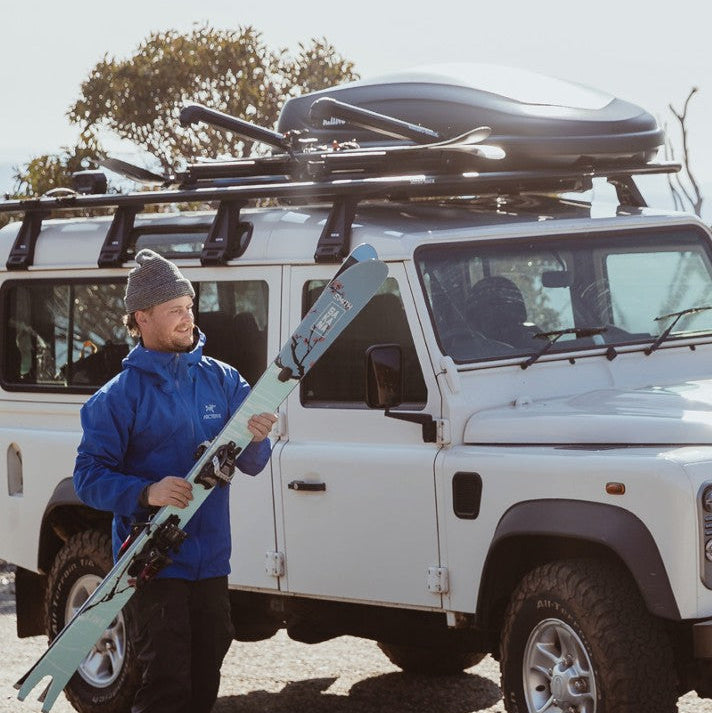 Person holding skis next to a white SUV with roof racks