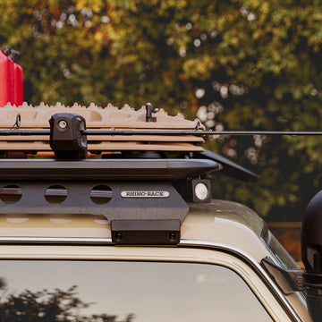Roof rack system on a vehicle with a red container and black toolbox against a blurred natural background