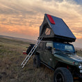 Jeep with a rooftop tent in a field at sunset