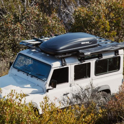 White SUV with a roof rack and cargo box in a forested area