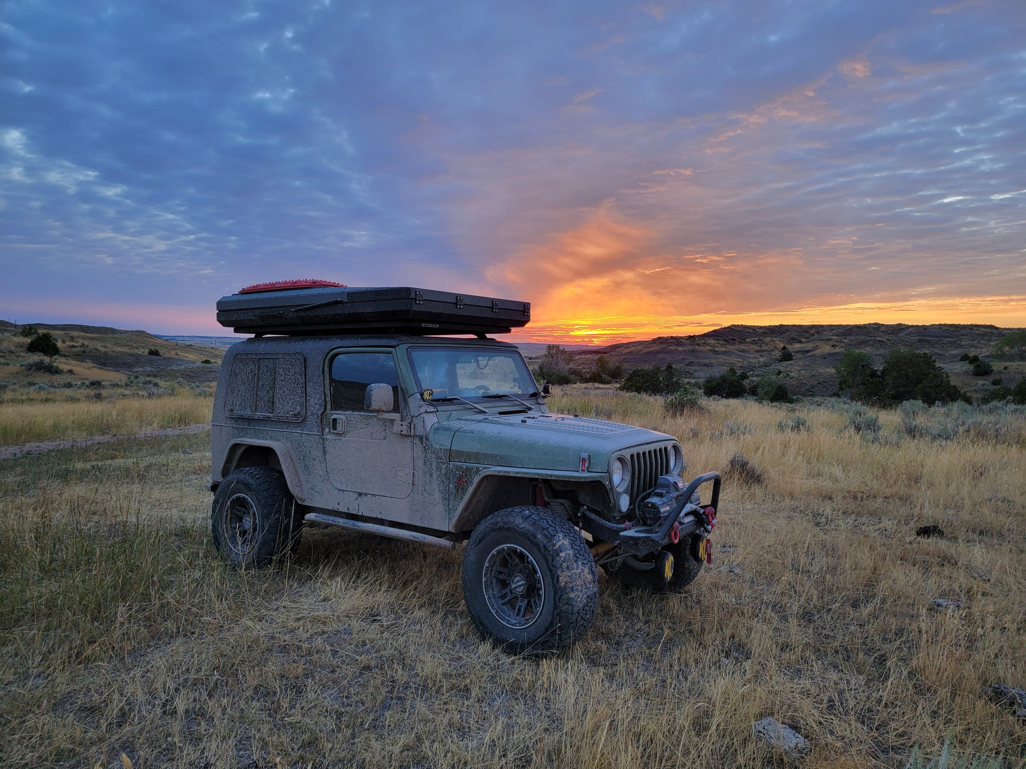Jeep with roof rack in a field at sunset