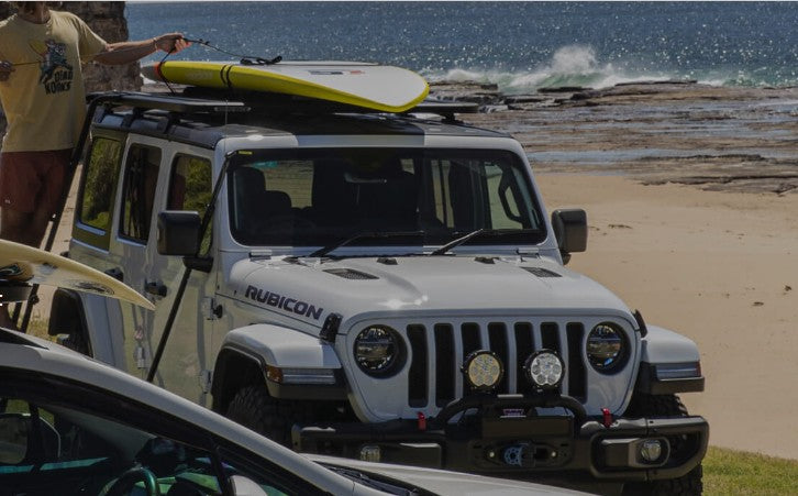 White Jeep with surfboard on top with Rhino Rack mounting spots
